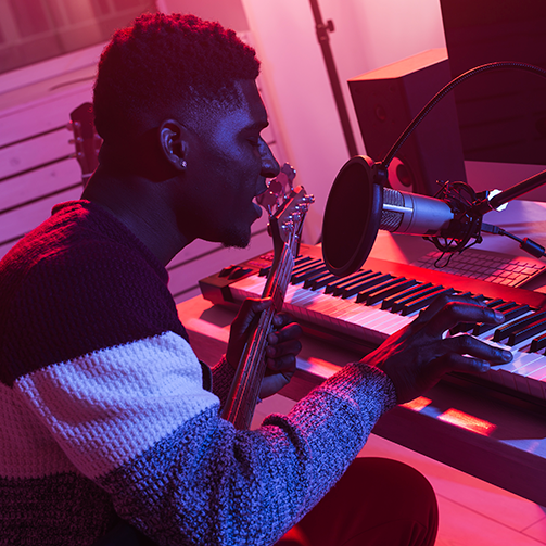 Junger Man sitzt mit Gitarre am Keyboard und singt